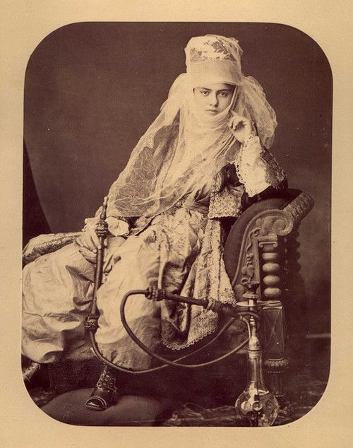 an old fashion photo of a woman wearing a veil and sitting on a chair with a cane in her hand