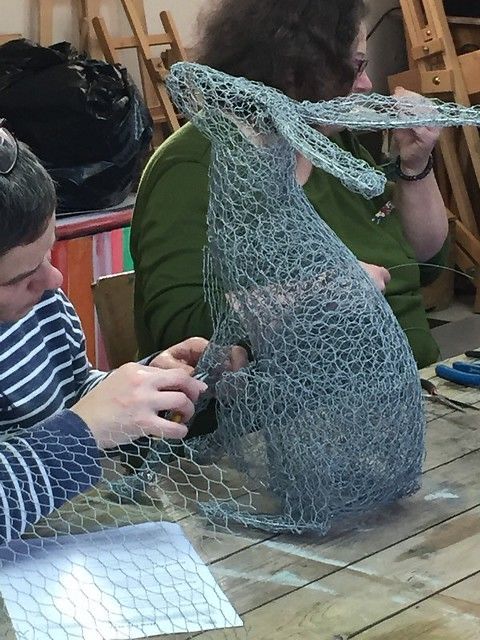 two people sitting at a table working on some kind of thing that is made out of chicken wire