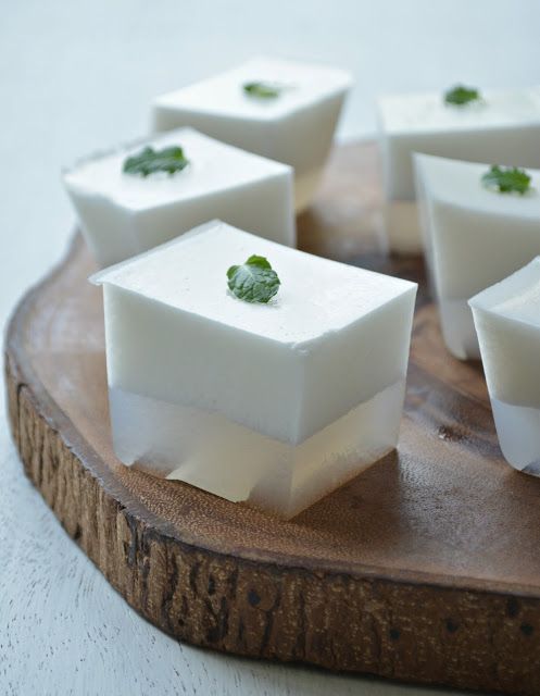 several cubes of food with green leaves on them sitting on a wooden plate,