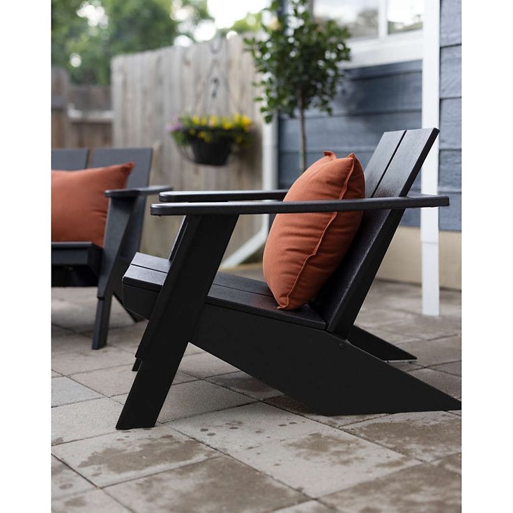 two chairs sitting on top of a patio next to a table with an orange pillow