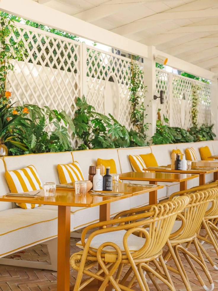 an outdoor seating area with yellow and white chairs, tables and plants on the wall