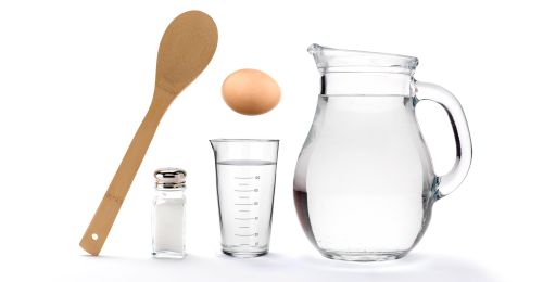 a pitcher, measuring glass and wooden spoon next to an egg on a white background