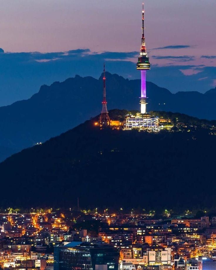 a view of a city at night from the top of a hill with mountains in the background