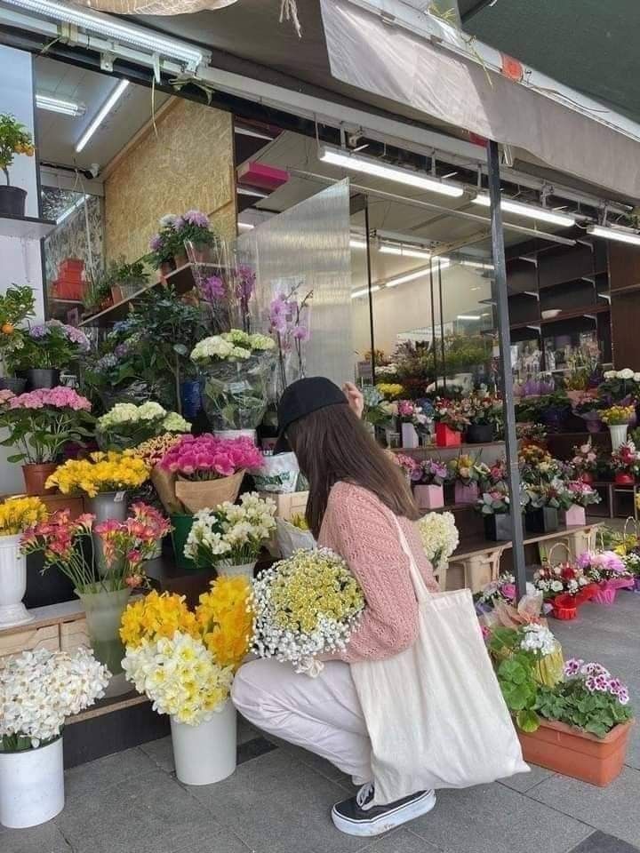 a woman kneeling down in front of a flower shop with lots of flowers on display