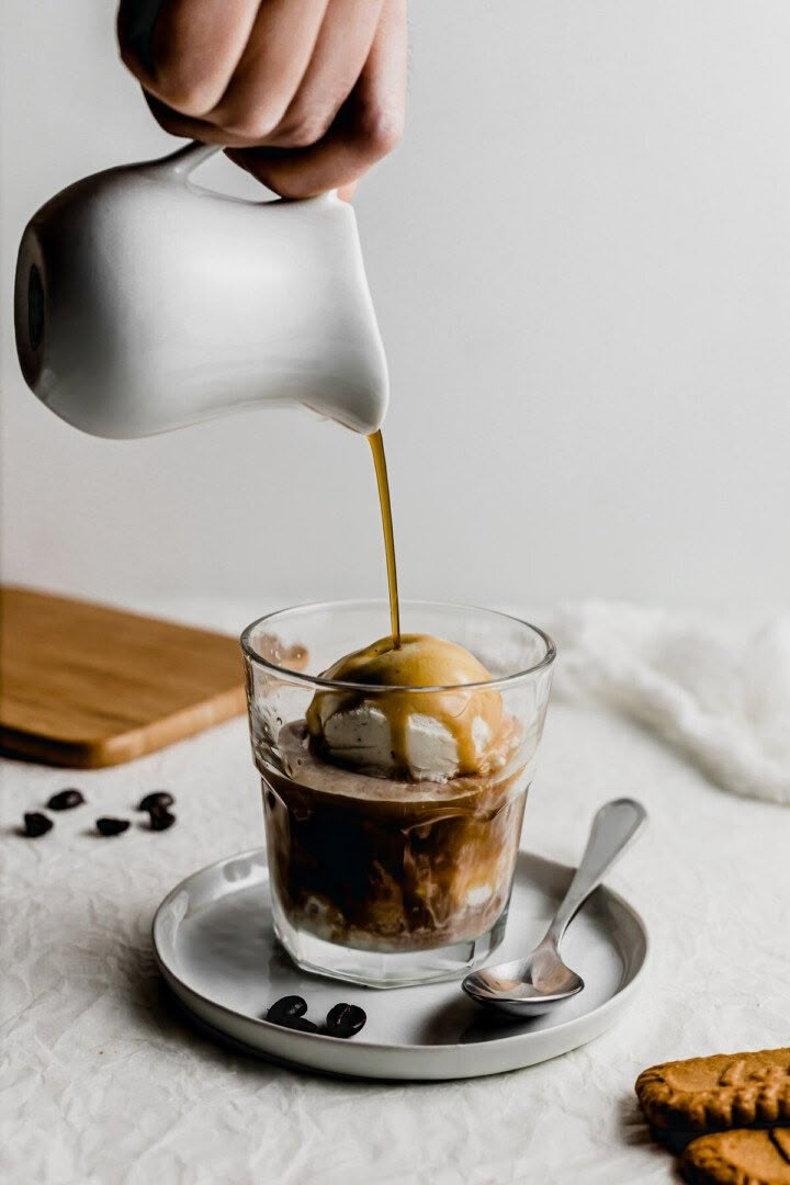 a person pouring ice cream into a glass with cookies on the table in the background