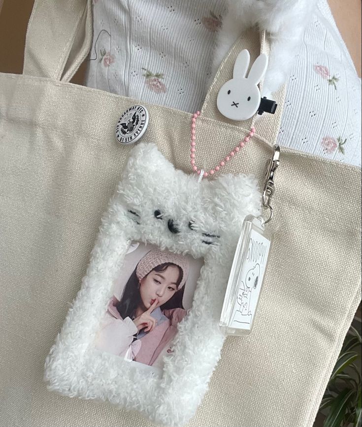 a white teddy bear holding a photo on a tote bag with a pink bead necklace