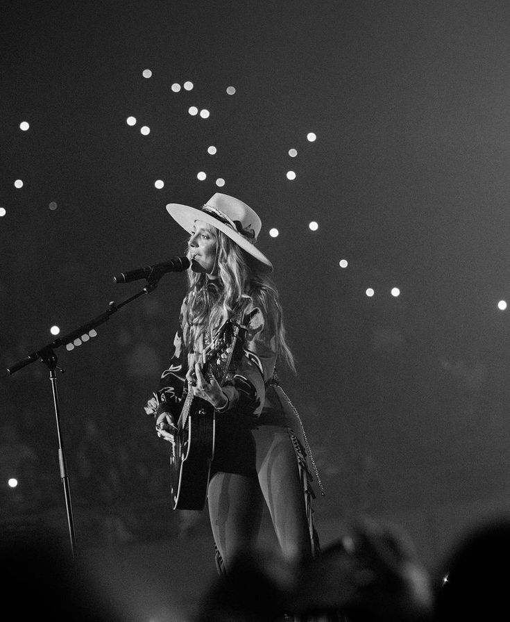 a black and white photo of a woman with a hat on singing into a microphone