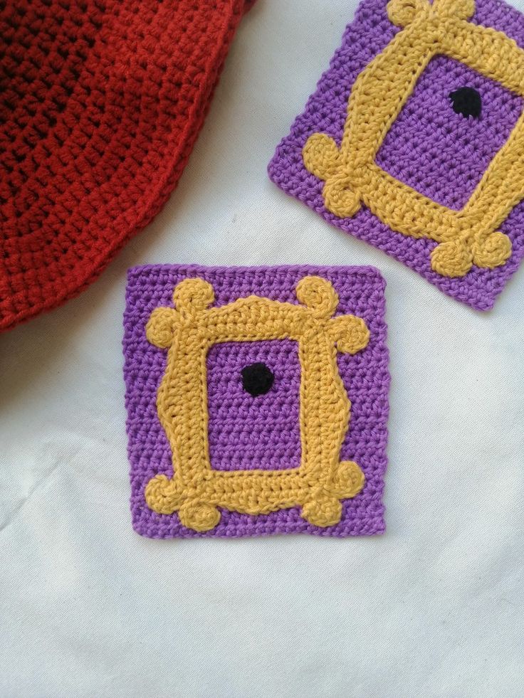 two crocheted square coasters sitting on top of a white table next to a red and yellow tie