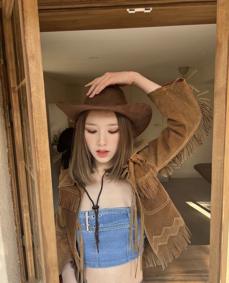 a young woman wearing a cowboy hat standing in a doorway with her hands on her head