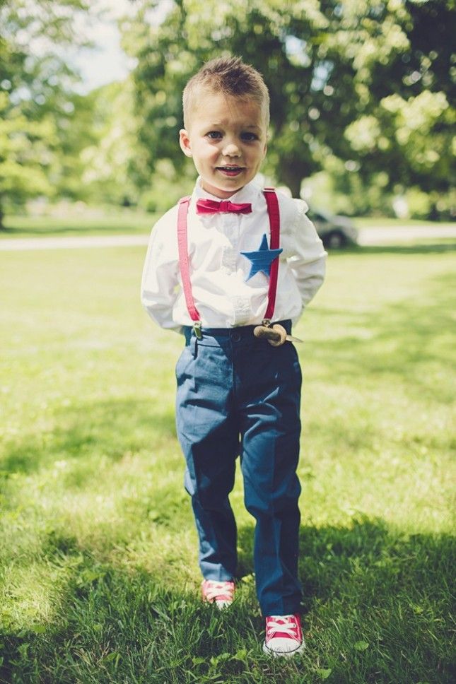 a young boy wearing a red bow tie and suspenders standing in the grass with his hands in his pockets