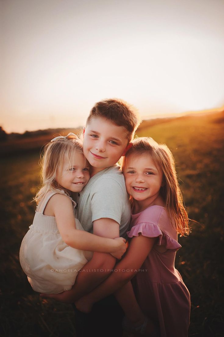 three young children hugging each other in a field with the sun shining down on them