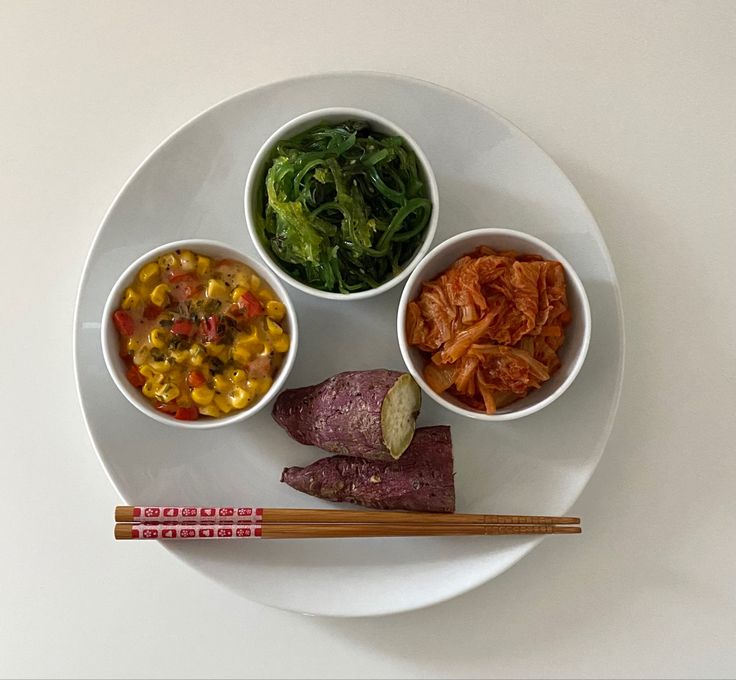 a white plate topped with three bowls filled with different types of food next to chopsticks