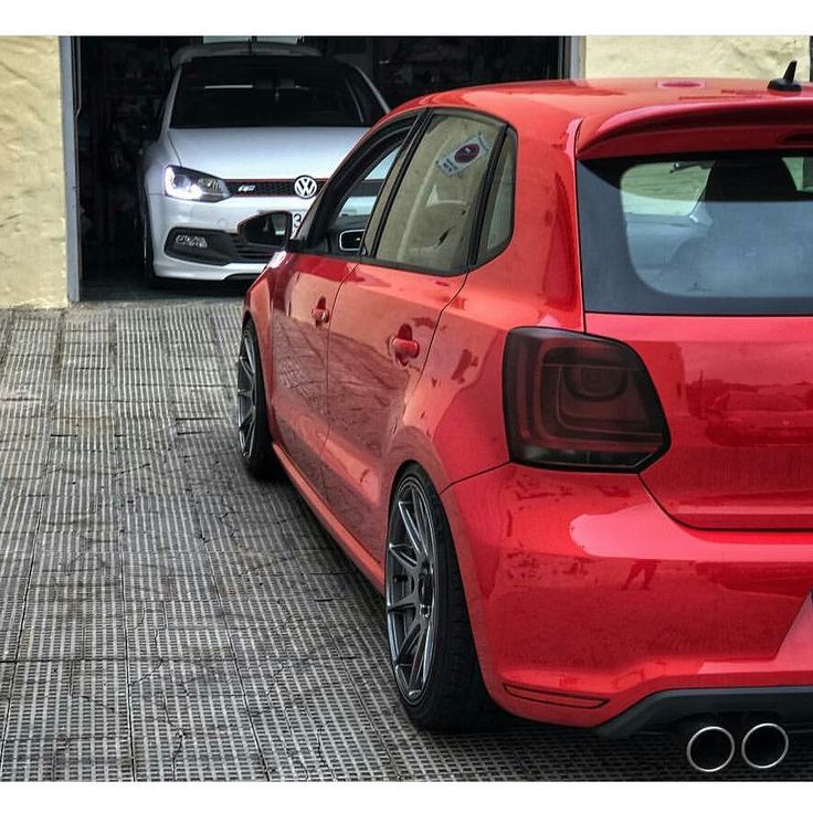 the rear end of a red car parked in front of a building with two other cars