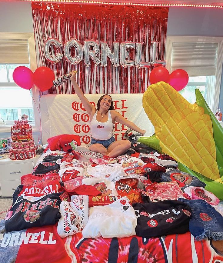 a woman sitting on top of a bed with lots of shirts and balloons in front of her