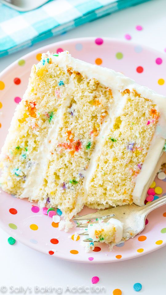 a slice of cake with white frosting and sprinkles on a pink plate