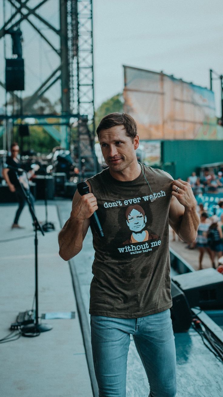 a man standing on top of a stage holding a microphone in his right hand and wearing a t - shirt that says don't even watch while he sings