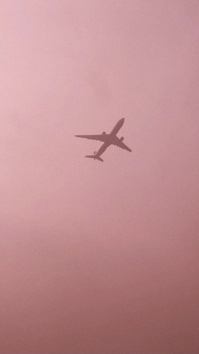 an airplane is flying in the sky on a foggy day with pink skies behind it