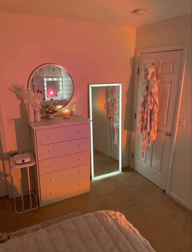 a bedroom with a dresser, mirror and lights on it's side table in front of the door