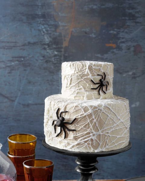 a three tiered cake decorated with black spider webs and glasses on a table