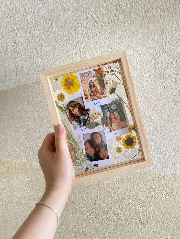 a person holding up a wooden frame with pictures on it in front of a white wall