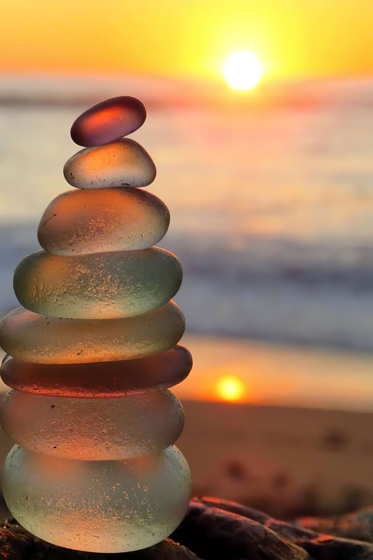 a stack of rocks sitting on top of a beach next to the ocean at sunset