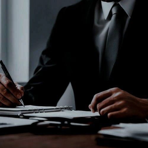 a man sitting at a desk writing on a piece of paper with a pen in his hand