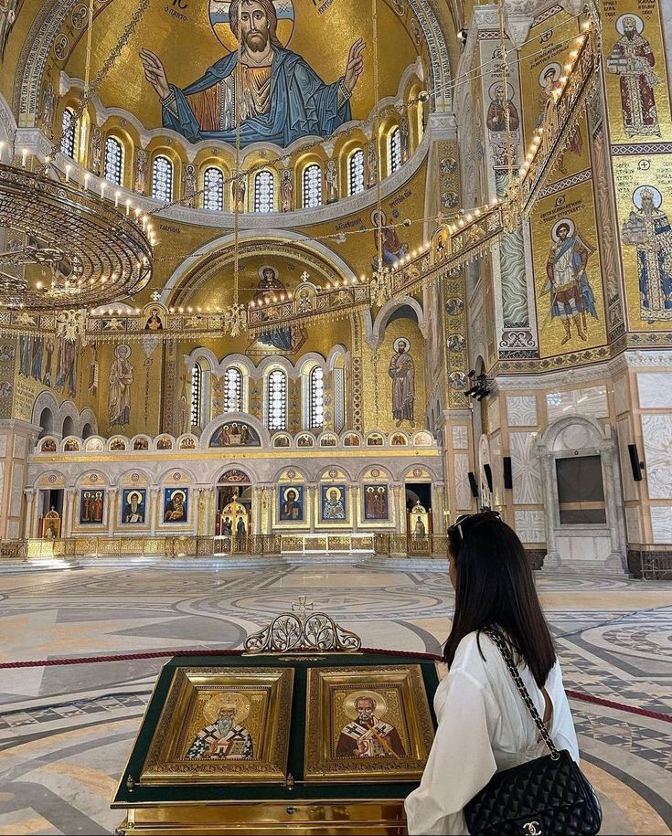 a woman standing in front of a golden and white church with paintings on the walls