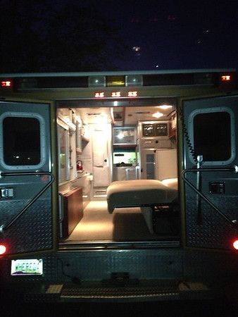 the interior of an ambulance at night with its doors open and seats in place to sit