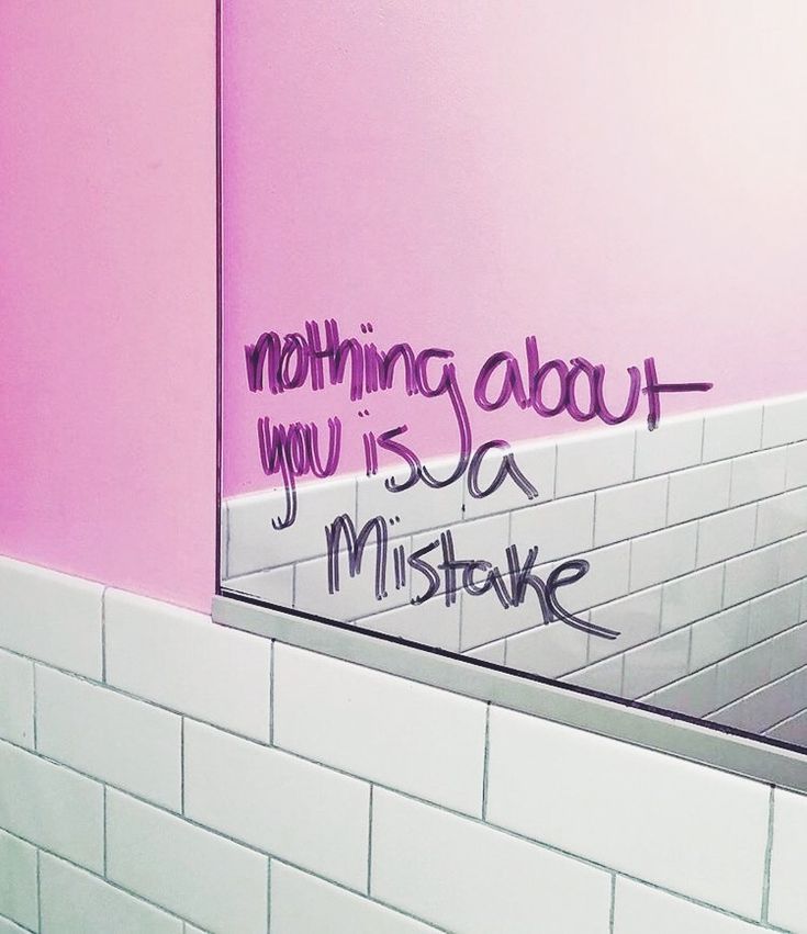 a bathroom with pink walls and white tile on the wall, has graffiti written on the mirror