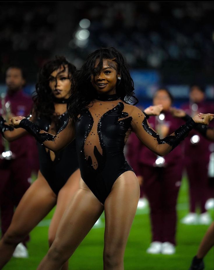 two women in bodysuits are performing on the field with other people behind them