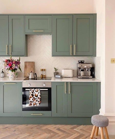 a kitchen with green cabinets and white counter tops is pictured in this image, there are flowers on the stove