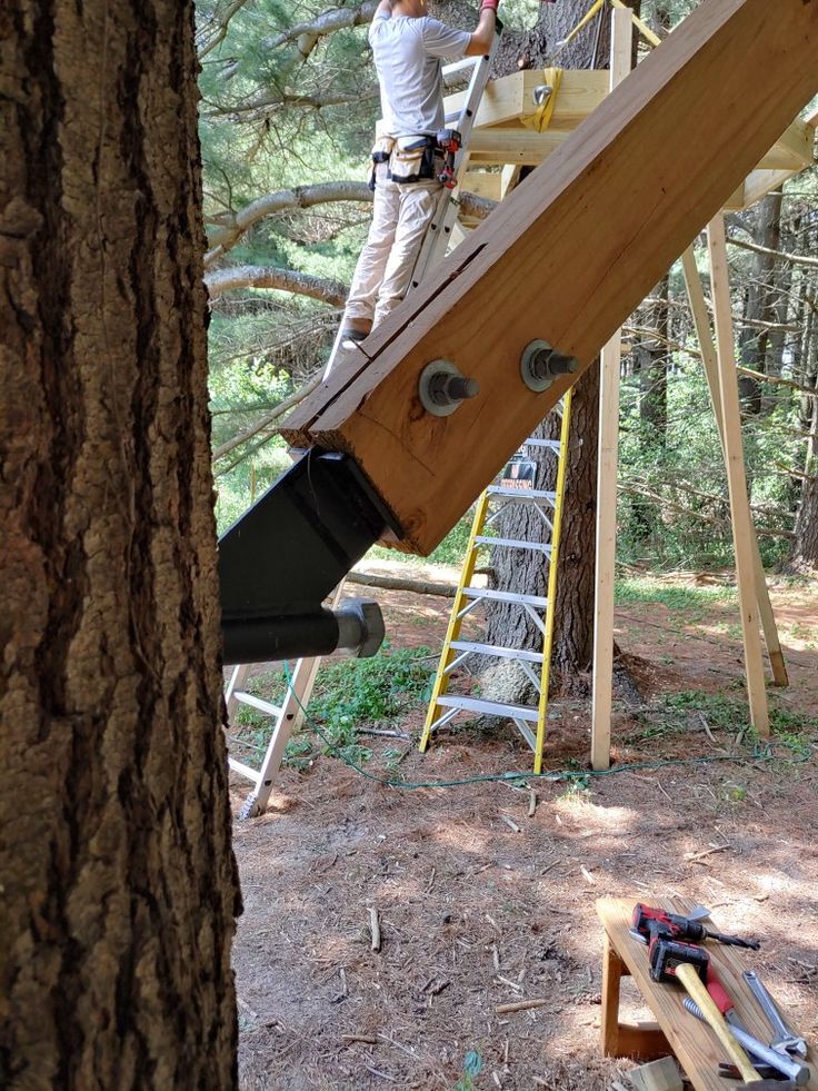 two men are working on a wooden structure in the middle of a forest with ladders