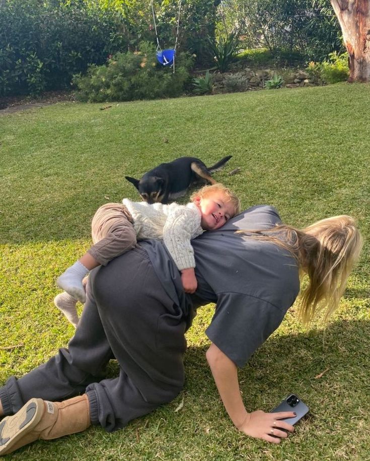 a woman and child playing with a dog on the grass