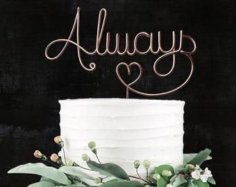 a white cake with greenery and the word always on top is sitting in front of a black background