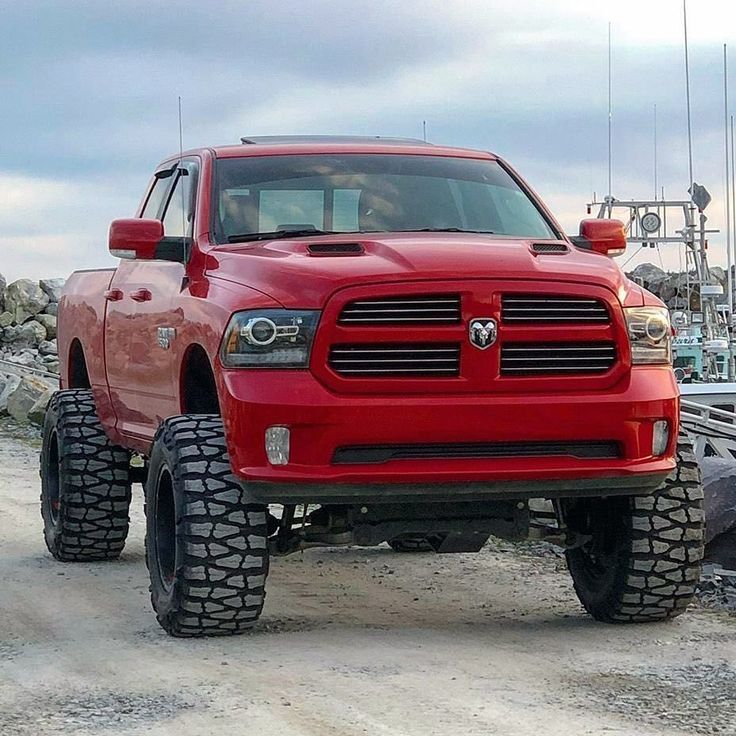 a red ram truck parked on top of a dirt road next to a boat dock