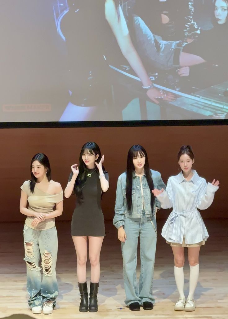 four girls standing on stage in front of a projector screen with their hands up