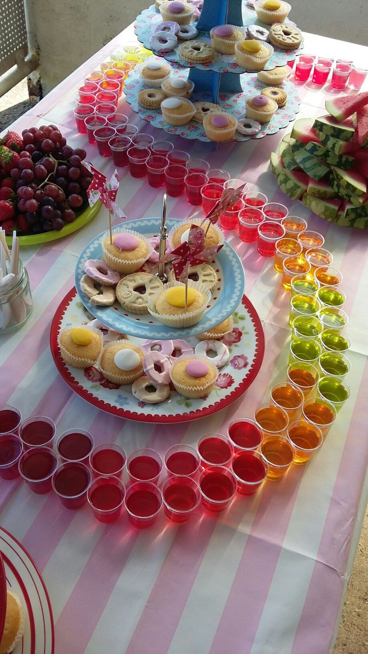 a table topped with lots of cupcakes next to cups filled with fruit and cake