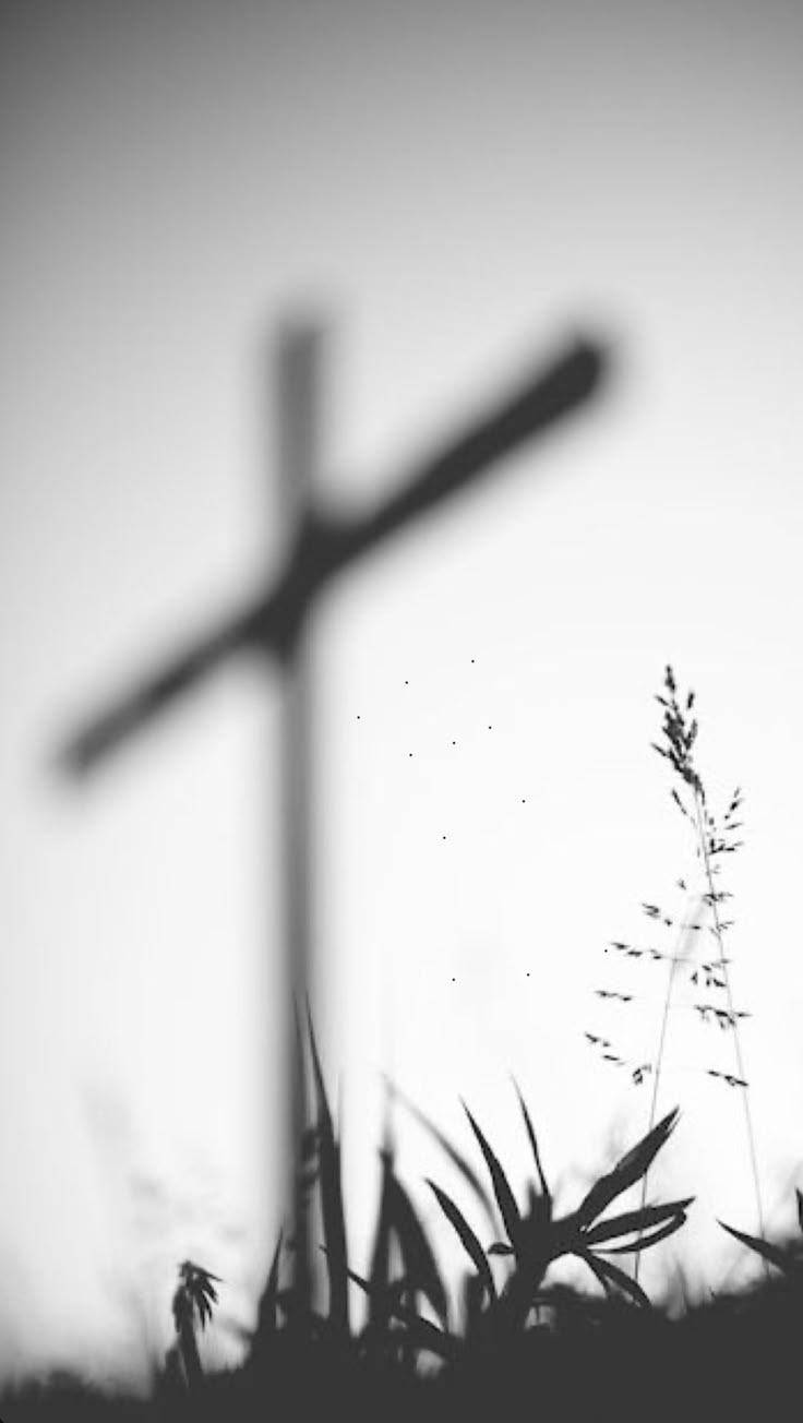 black and white photograph of a cross in the distance with grass behind it, silhouetted against a gray sky