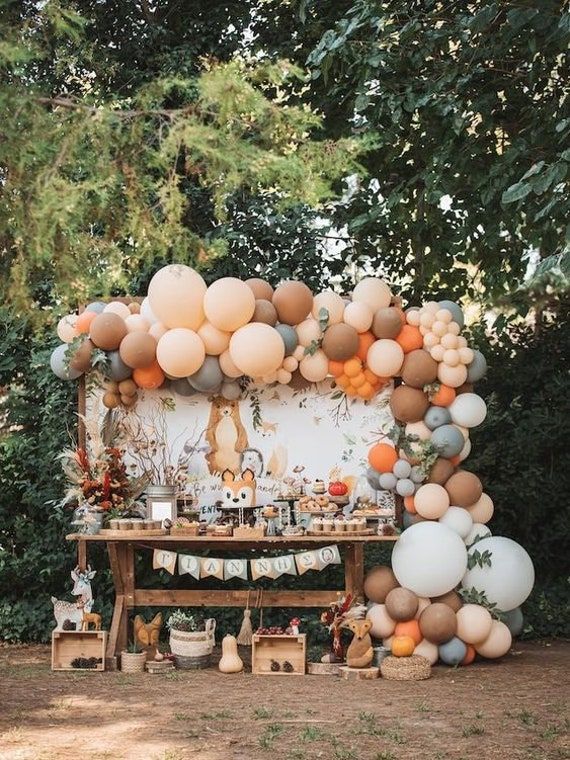 an outdoor party with balloons and decorations on the table, in front of some trees