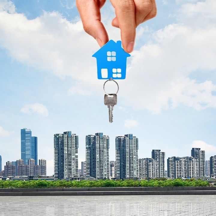 a hand holding a house shaped key in front of a cityscape with skyscrapers