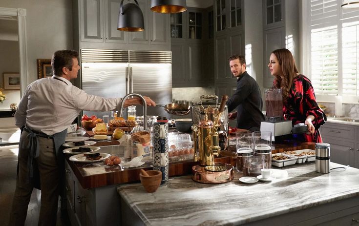 three people standing around a kitchen island with food on it