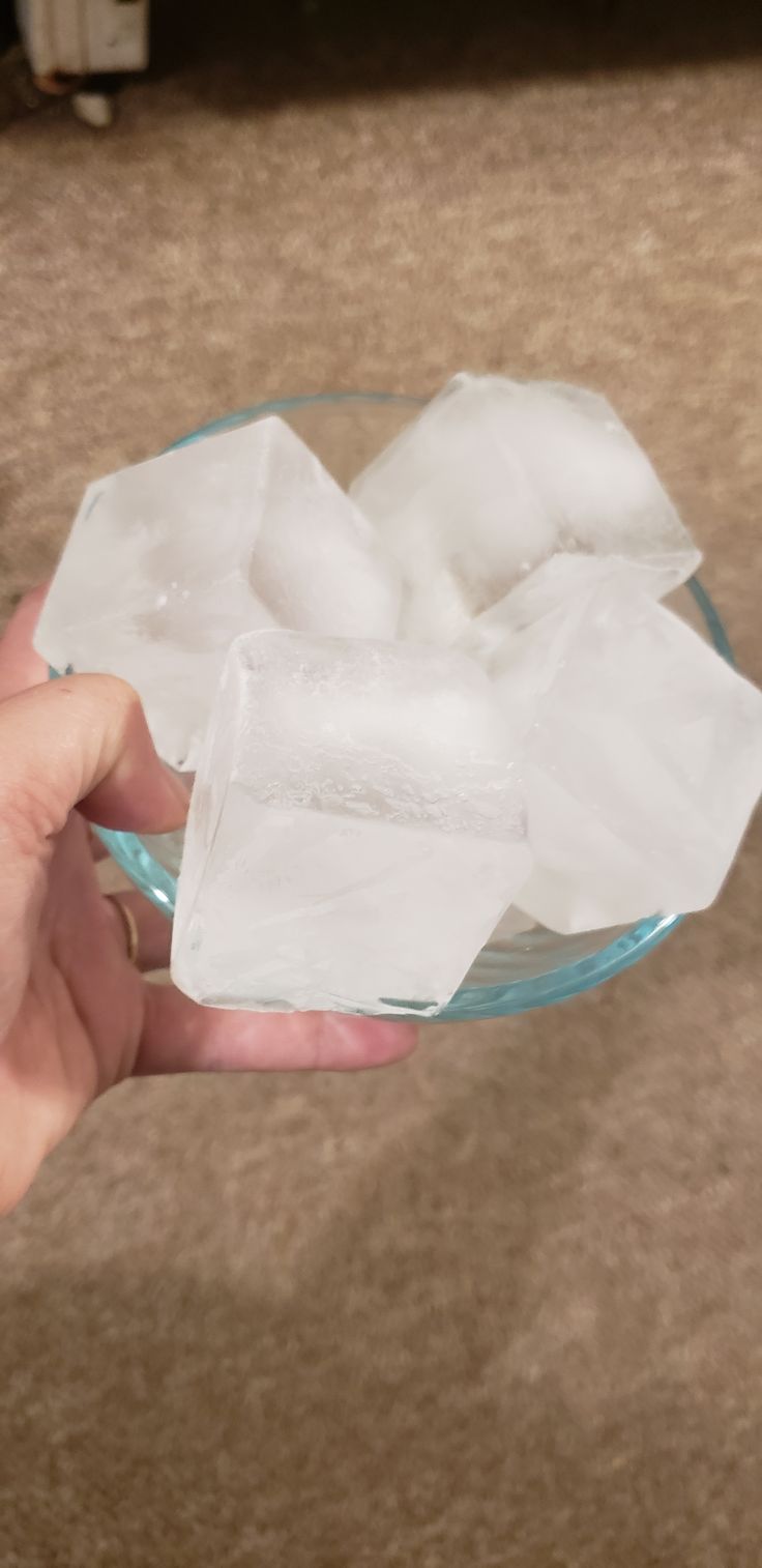 a person holding a glass bowl filled with ice cubes on top of a carpeted floor