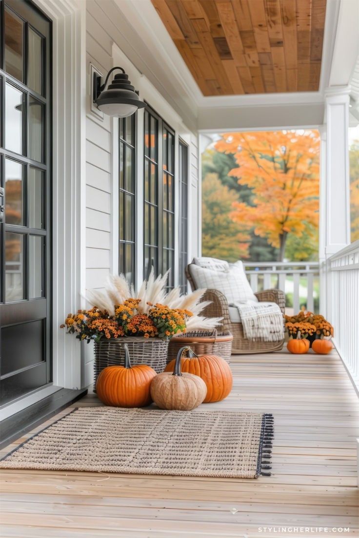 a porch decorated with pumpkins and fall foliage