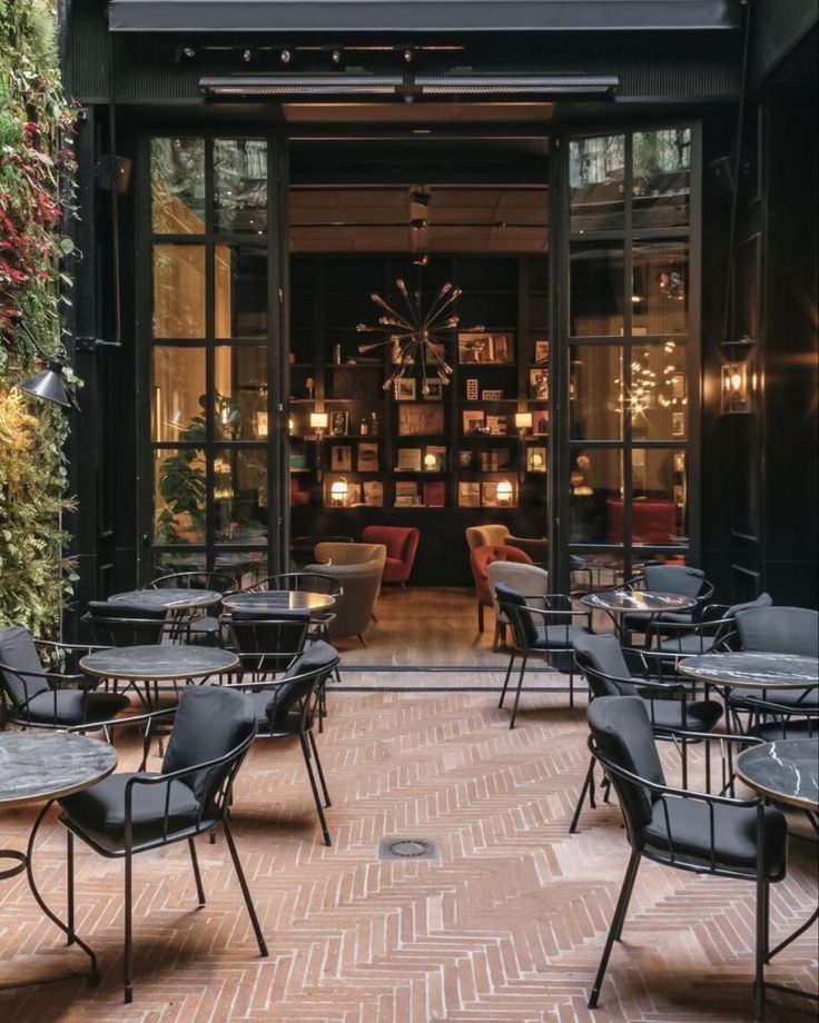 tables and chairs are set up in front of the entrance to a restaurant with plants growing on the wall