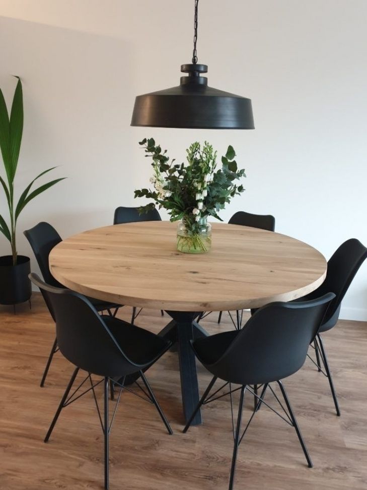 a round wooden table surrounded by black chairs and a potted plant in the center