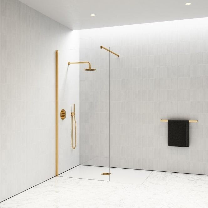 a white tiled bathroom with gold fixtures and black towels hanging on the shower wall next to it