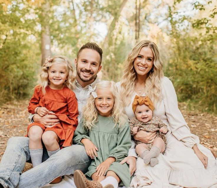 a man and two women are sitting on a blanket in the woods with their children