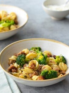 two bowls filled with pasta and broccoli on top of a gray tablecloth