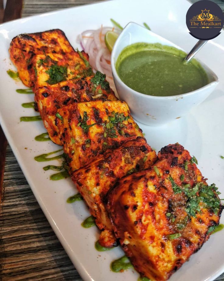 some food is sitting on a white plate with a green dipping sauce in the bowl