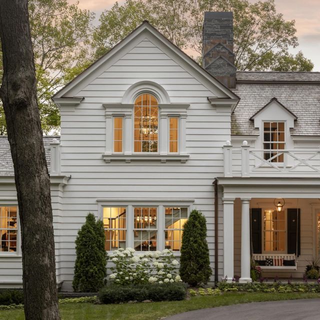 a large white house with lots of windows and bushes in front of the house is lit up at night